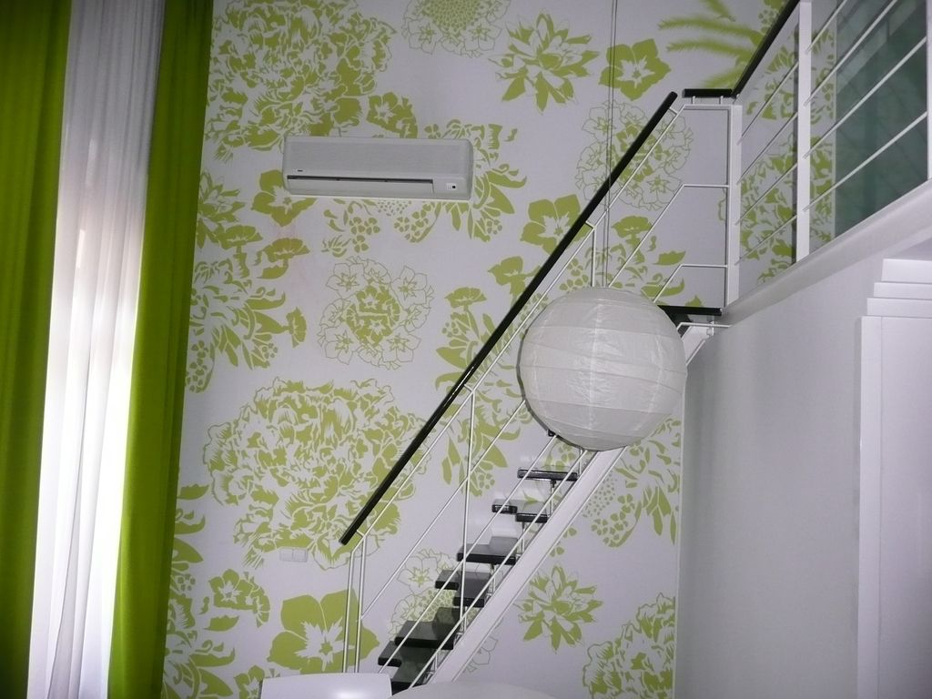 A slim steel staircase with open treads rising past a green and white patterned wall