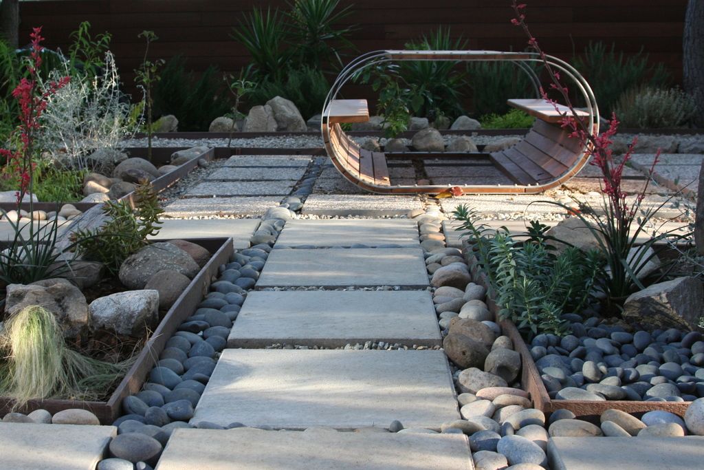 A modern garden path of concrete pavers edged with river stones and planting