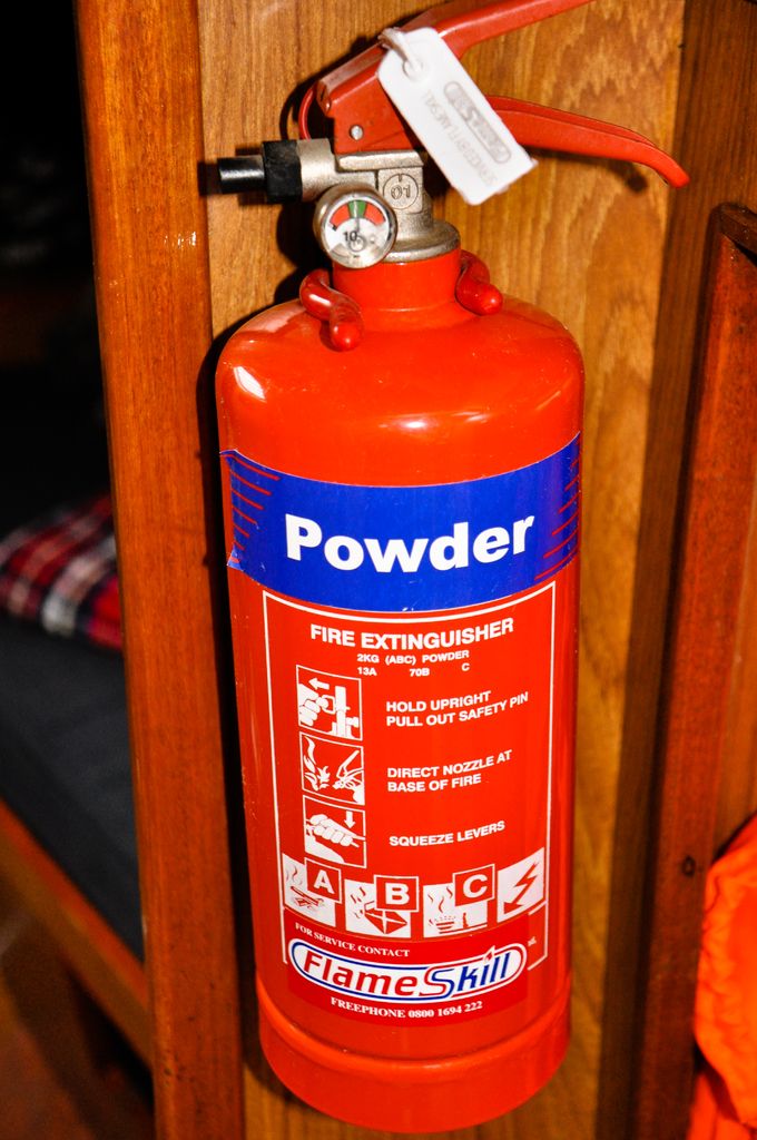 A red powder fire extinguisher hung on a wooden wall bracket