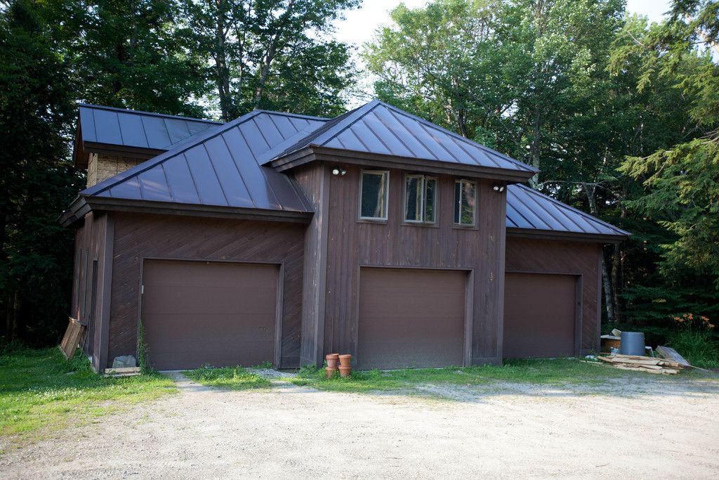 A dark standing seam metal roof on a timber garage surrounded by trees