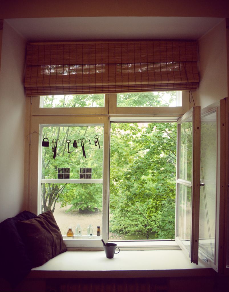 An open casement window above a cushioned window seat with green trees outside